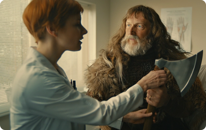A hand specialist in a clinic examines a patient dressed in Viking-style clothing who is holding an axe.